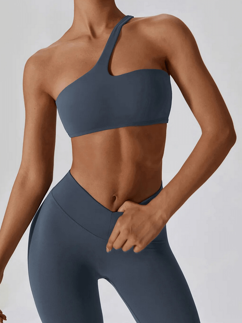 Female model wearing sports one shoulder push-up bra and leggings set SF1697 in dark blue. Stylish and breathable workout wear.